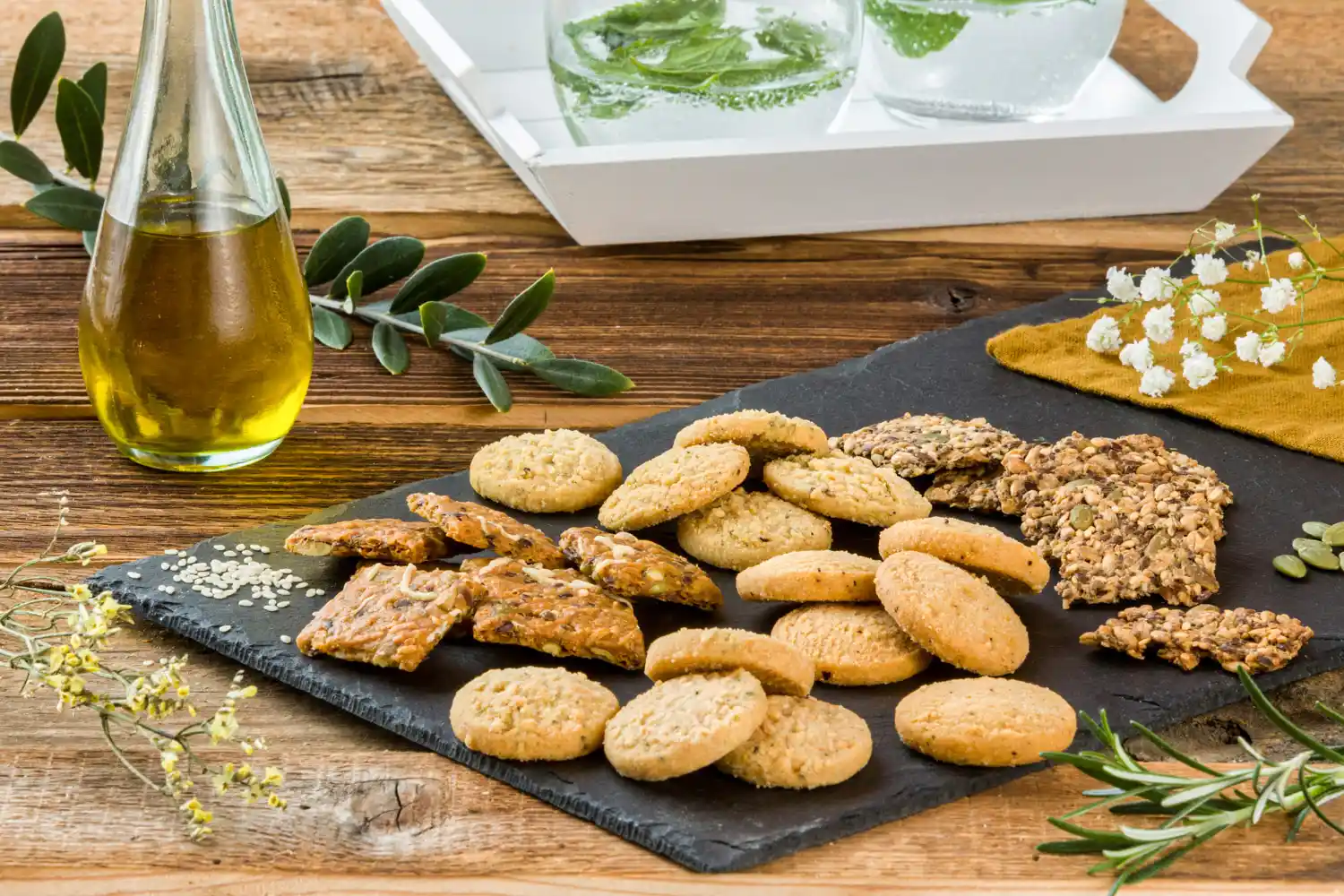 Mise en situation des petits biscuits salés avec un peu d'huile d'olive dans un flacon et des boissons sur un plateau.